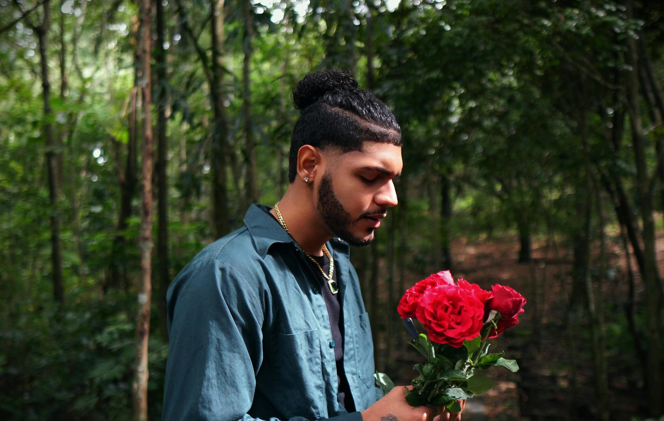 Man with roses in hand, standing in a tranquil forest environment.