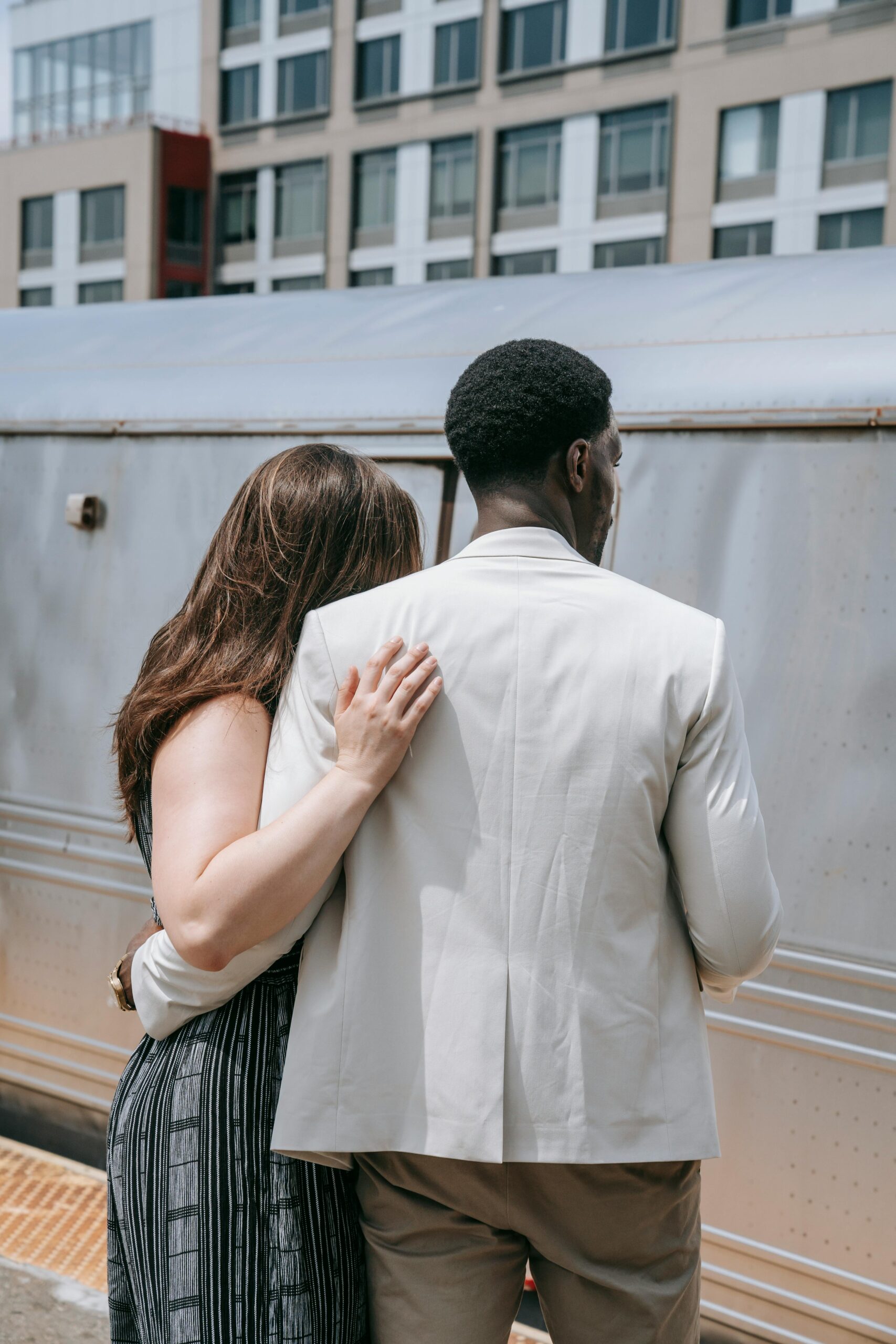 Interracial couple standing together at a train station, back view, in a candid moment.