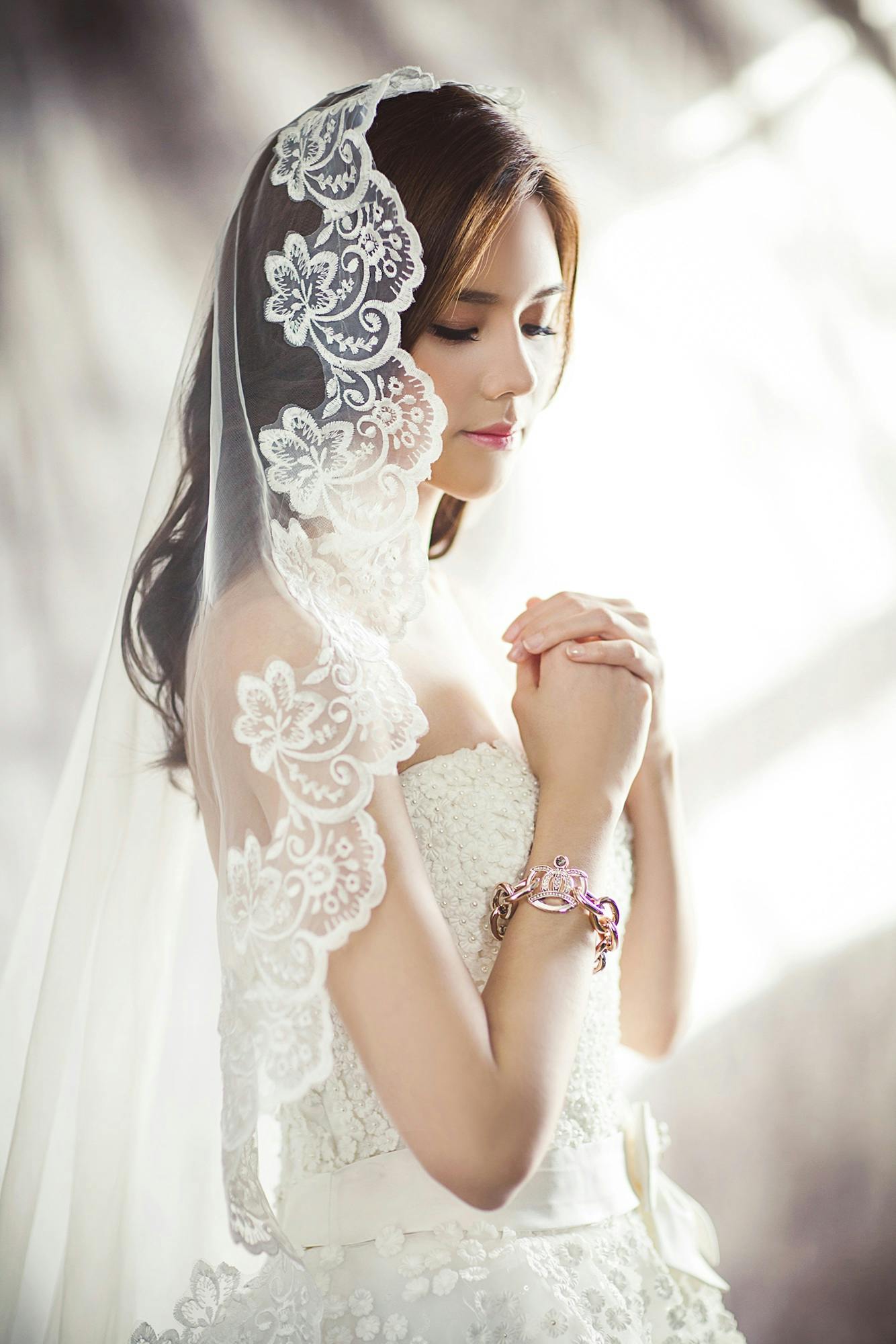 Beautiful bride in lace gown and veil, captured in soft lighting.